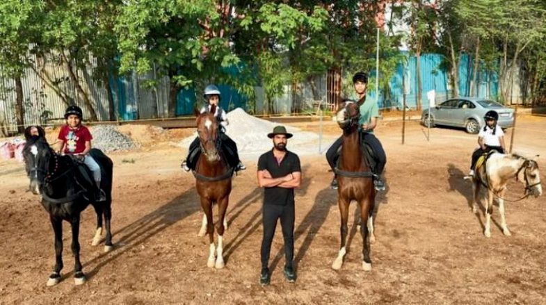 Trainer standing with three horses and riders in an outdoor arena